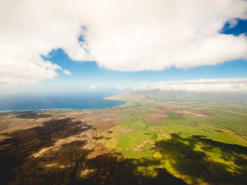 a photo taken from high above, the ground is green and the seaside is far away. there are some clouds in the sky.
