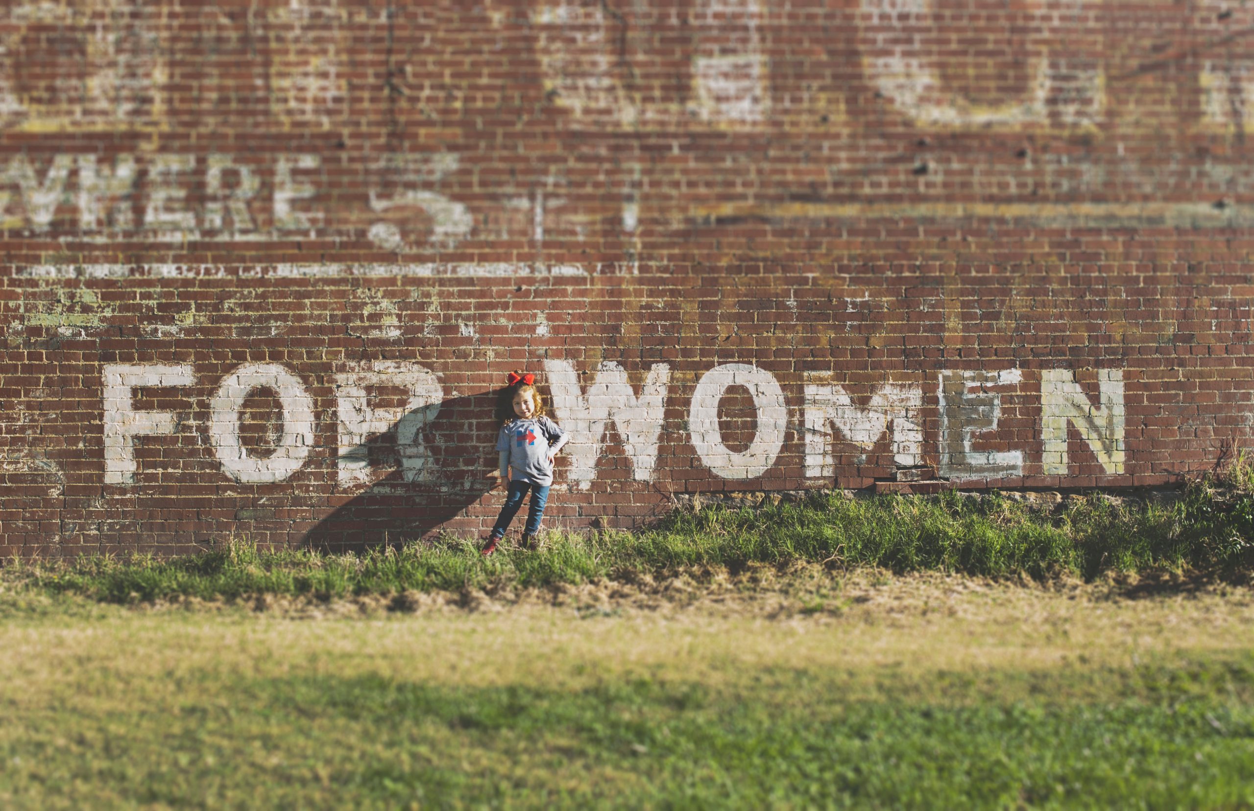 girl standing in front of brick wall with the words For Women painted over it