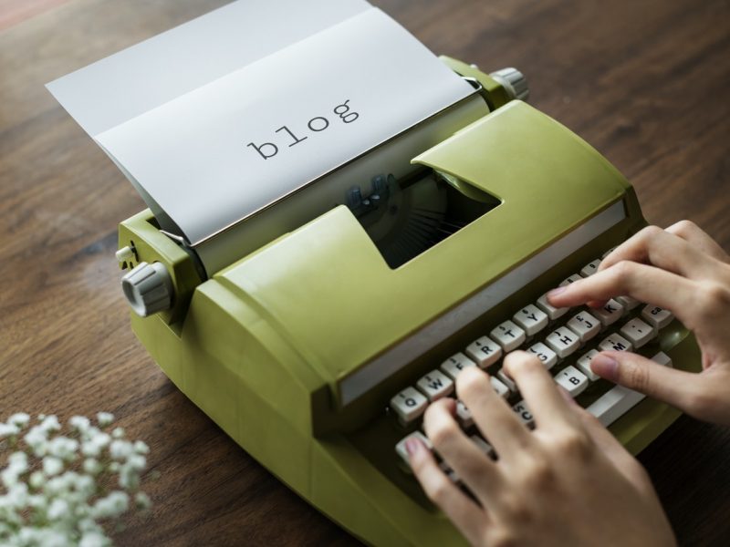 photo of a person using a green typewriter, a paper still inside says 'blog'