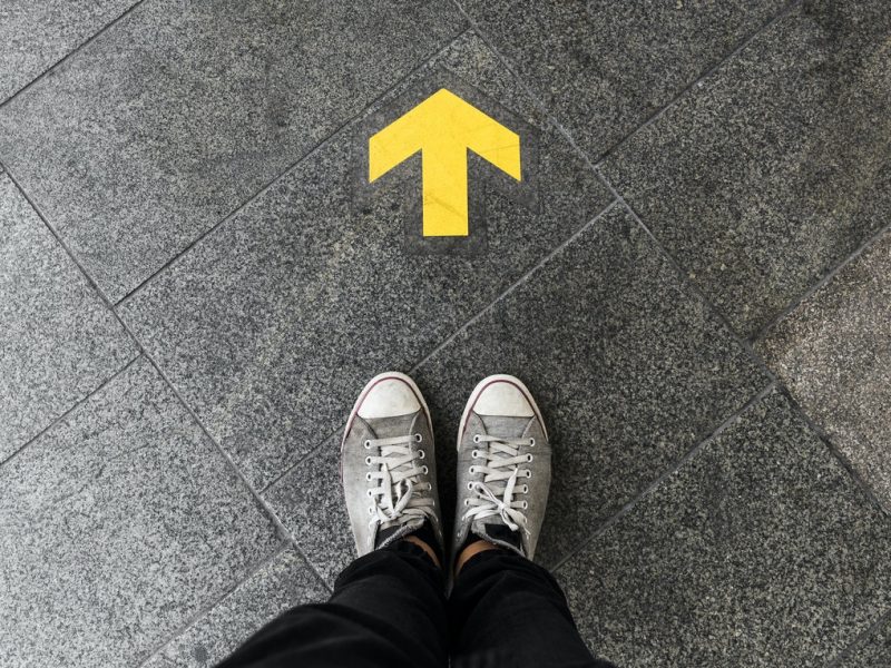 a person standing near a yellow arrow pointing forward, painted on the pavement