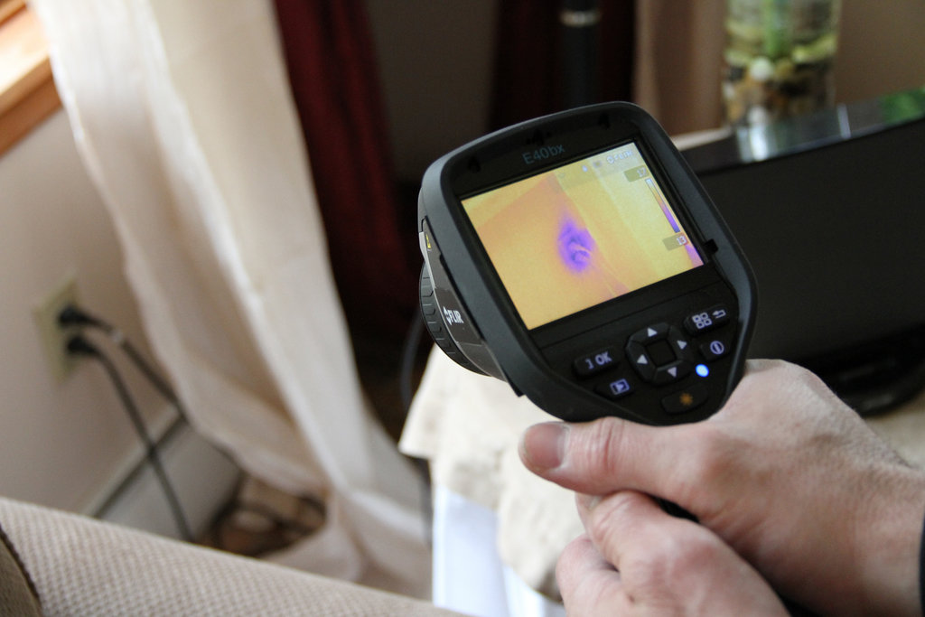 A person is holding a device that is pointing to a plug. the device's monitor reveals a purple colours around the plug, as it energy was 'leaking'