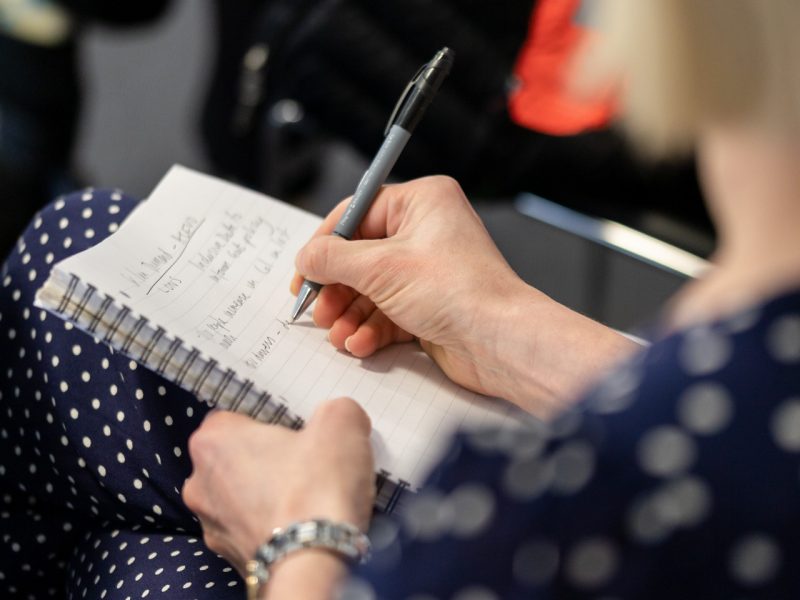 A close up photograph of woman writing in a pad with a pen