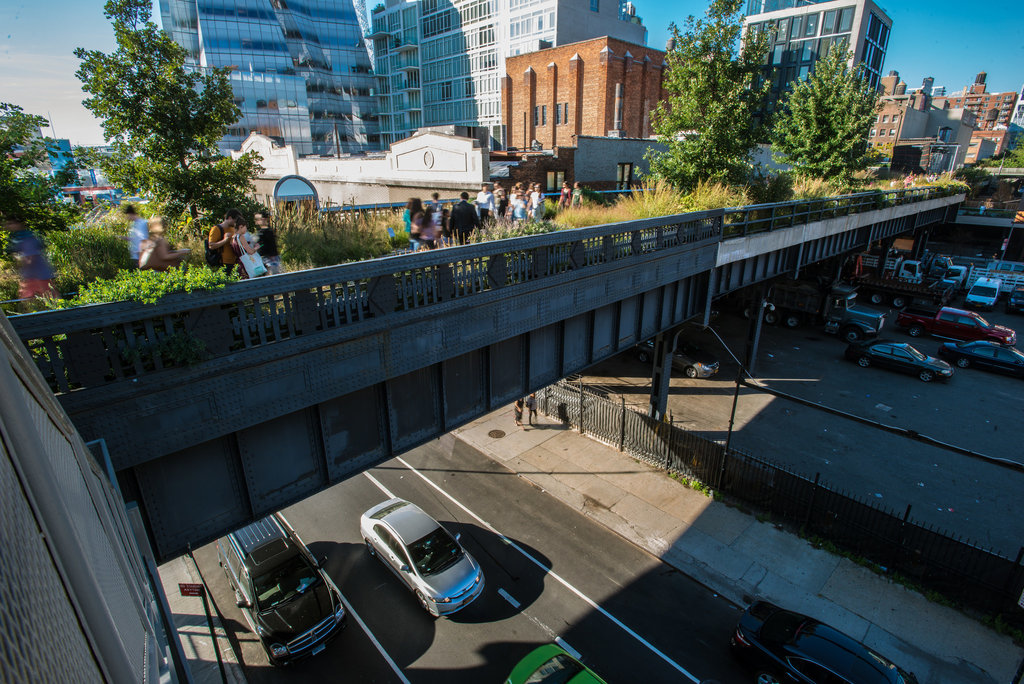 High Line in New York. A pedestrian bridge transformed into a park, people are walking around and admiring the greenery, while cars pass underneath