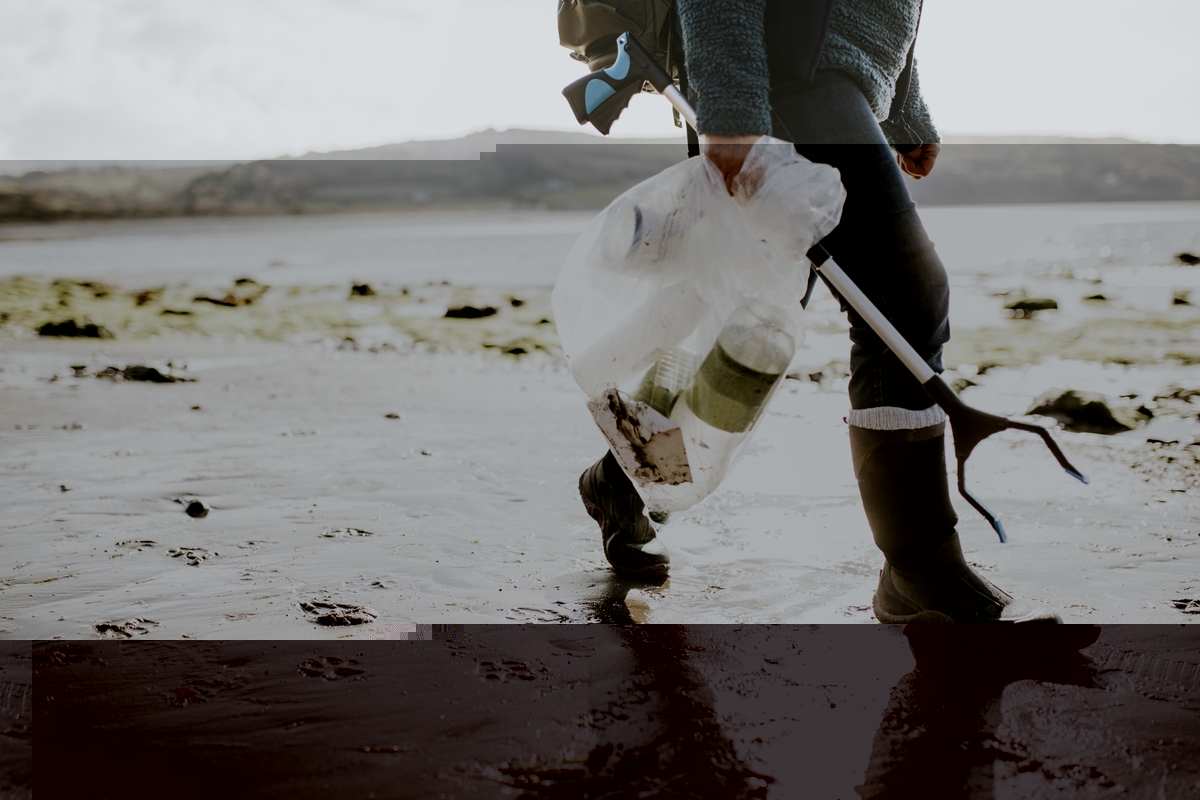 person walking on a beach carrying a device to pick litter and a plastic bag to put litter inside