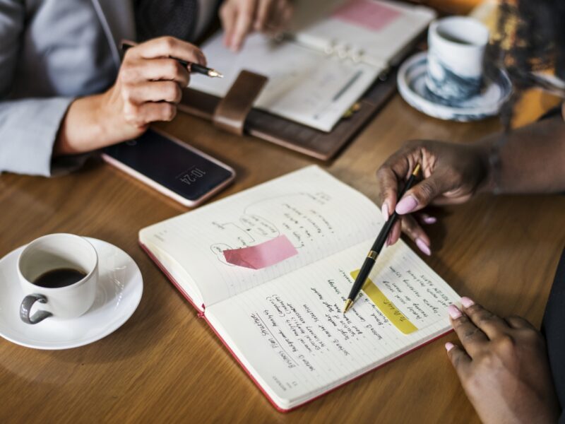 photo of two people having a meeting. they are looking at a notebook and having coffee
