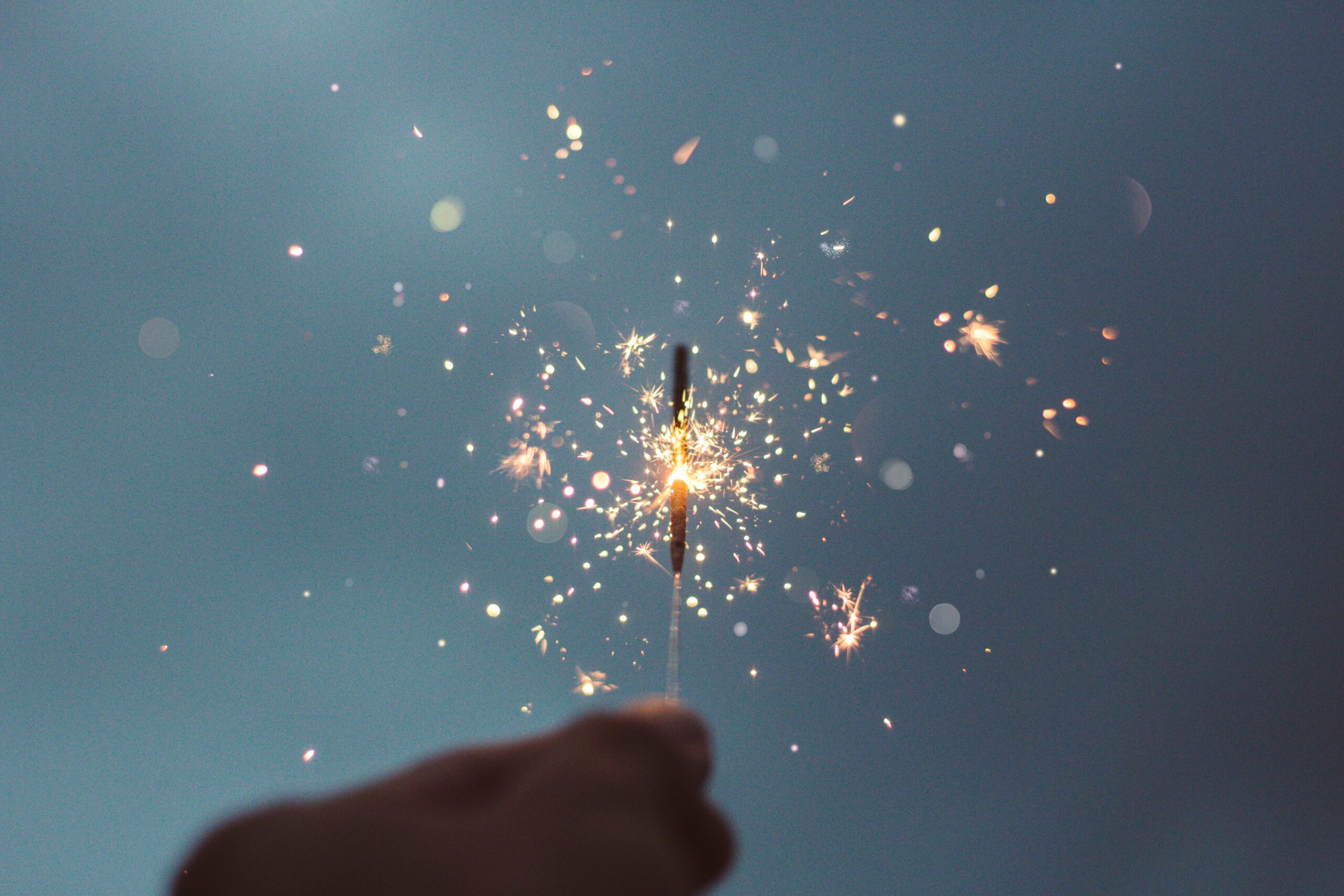 Hand holding a sparkler against a cloudy background