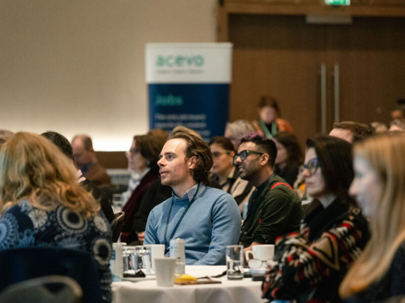 A photo of people sat at tables in a conference room