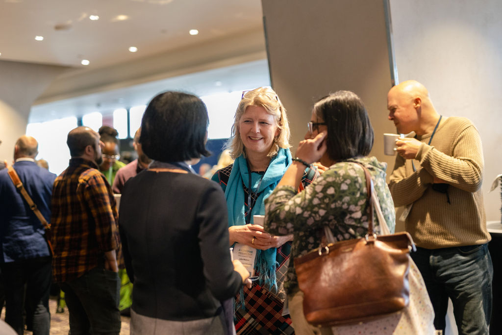 three people having lively chat in a public area, there are more people in the background, it is a casual gathering and networking