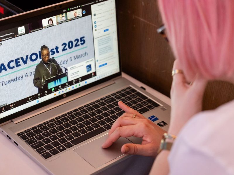 Person looking at their laptop, watching someone speak