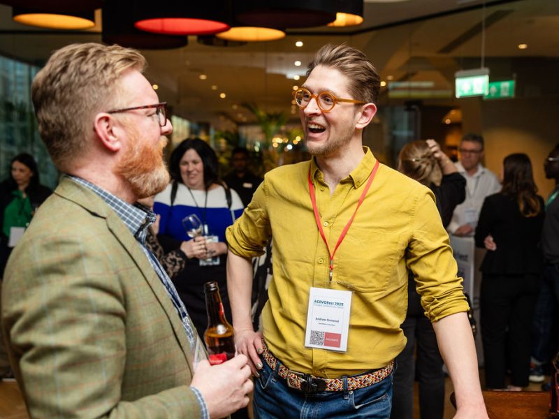 A photograph of two men stood smiling in conversation