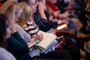 person with a notebook open on their lap, taking notes during a conference