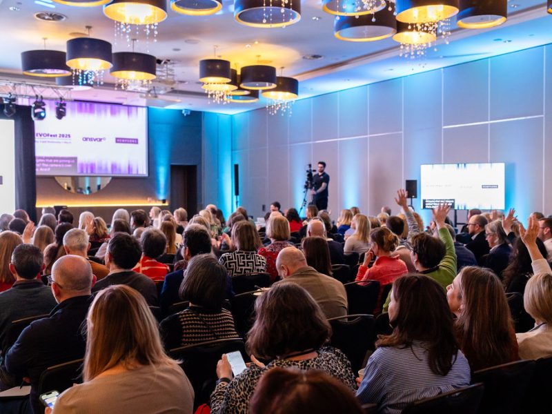 photo of the inside of a conference hall. people are seated, looking at the stage, where the speakers are