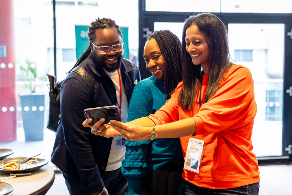 three people standing next to each other. one of them is holding a mobile phone and taking a selfie of them