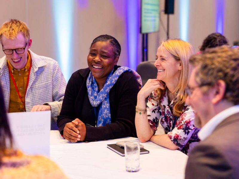 four people sitting around a table, having a chat, and having fun. they are smiling